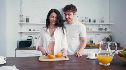 Man kissing woman in bra and shirt during breakfast in kitchen 
