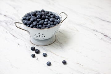 Fototapeta na wymiar Freshly Picked Blueberries in a White Colander on a White Countertop