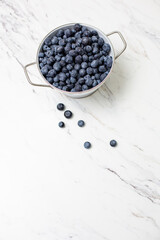 Top View of Freshly Picked Blueberries in a White Colander on a White Countertop