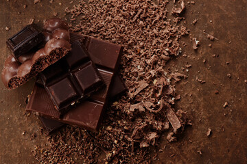 Composition of bars and pieces of different milk and dark chocolate, grated cocoa on a brown background top view close up