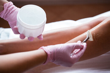 Photo of hands in pink medical gloves applying a cooling cosmetic gel with a brush. Preparing the skin for the procedure