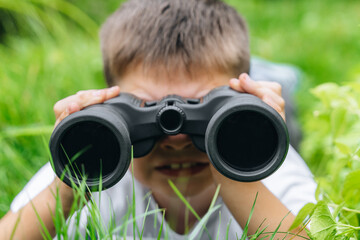 child boy in white t-shirt looking through binoculars in nature green landscape. Explore and discover wildlife concepts. kid adventure, searching for direction. imagination, freedom. copy space