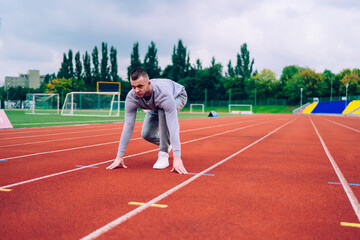Fototapeta premium Handsome determined male runner standing on start point on stadium prepare for running distance, serious caucasian man athlete looking straight for begin fast cardio workout for reaching goals