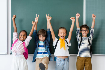 Fototapeta na wymiar Selective focus of multicultural classmates showing peace and yes gestures near chalkboard in classroom