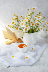 still life bouquet of field daisies in a vase, an old book and a cup of tea on a white background. bouquet of flowers in a vase