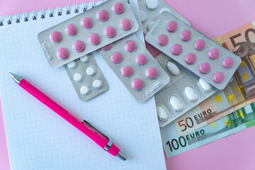 notepad with pills on table close up. money on pink background
