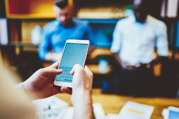 Cropped view of male hands typing text information on modern smartphone device with blank screen area for your website, selective focus on mobile gadget with copy space for business content