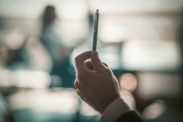 White man's hand holds a pen. Blurred office background. High quality photo.