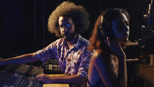 Music studio. Creative people. Hispanic man and woman working in the recording studio. The brunette curly couple is producing songs in comfortable environment. 