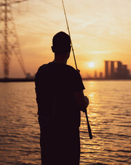 During the enchanting sunset, a young angler stands on the beach, casting their line while gazing...