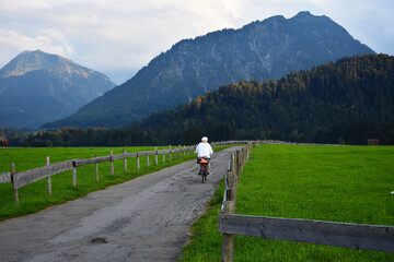 Fototapeta na wymiar an old lady with white dress cycling through Alp mountains near Oberstdorf on a green path