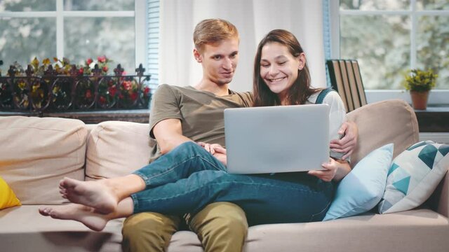 Young couple relaxing on couch with laptop in living room and kissing at home