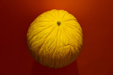 Yellow melon on dark red background. Top view, dramatic light. Creative food concept.