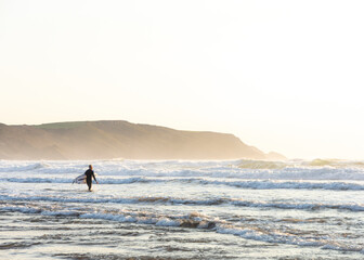 Fototapeta na wymiar Surfer Walking out into the Ocean - Bude, Cornwall, England