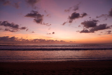 Naklejka na ściany i meble A dramatic sunset view on Kuta beach, Bali, with gradations of purple, orange and blue sky