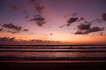 Fototapeta na wymiar A dramatic sunset view on Kuta beach, Bali, with gradations of purple, orange and blue sky