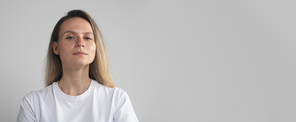 caucasian woman in white t-shirt, close up, expressing arrogance and confidence, against gray background. Girl is proud of her achievements looking down to camera