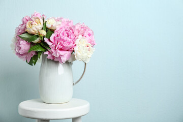 Beautiful peonies in jug on white stool against light blue background. Space for text