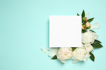 Beautiful white peonies and blank card on turquoise background, flat lay. Space for text