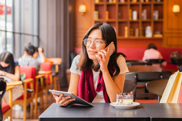 Lifestyle, Technology Concept - Happy Asian woman talking on the phone and using tablet computer in a coffee shop.