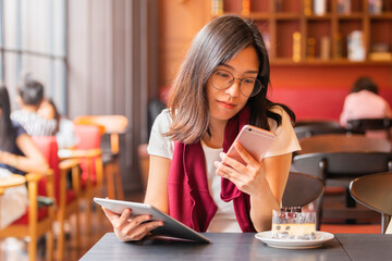 Lifestyle,Technology Concept - Relaxing after day shopping. Beautiful asian woman enjoying tablet computer and smartphone sitting at a table with cake, mobile phone in a coffee shop.