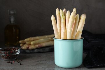 Fresh white asparagus in mug on grey table. Space for text