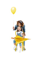 mother with yellow balloon standing near daughter on chair with umbrella isolated on white