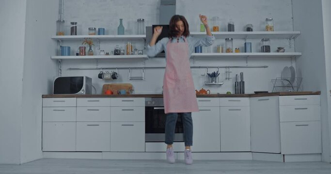Young woman in apron dancing in kitchen 