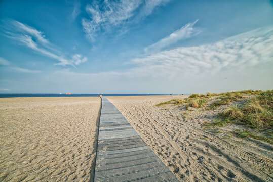 Amager Strand romantic wooden pathway or boardwalk on the beach leading to a calm Baltic Sea. Few people walk in the distance conveying relax, realisation concept. Way or path to success illustration