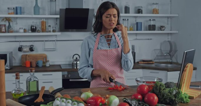 Woman wounding finger while cutting tomatoes in kitchen 