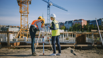 Naklejka premium Construction Worker Using Theodolite Surveying Optical Instrument for Measuring Angles in Horizontal and Vertical Planes on Construction Site. Engineer and Architect Using Tablet Next to Surveyor.