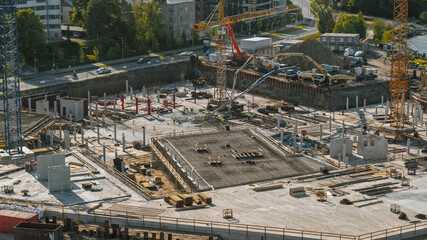 Aerial Shot of a New Constructions Development Site with High Tower Cranes Building Real Estate. Heavy Machinery and Construction Workers are Employed. City Houses in the Background.