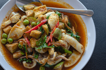 Close up at Stir fried squid with herb on white dish on black table background with nature light by window at seafood restaurant, Thailand seafood, Selective focus.
