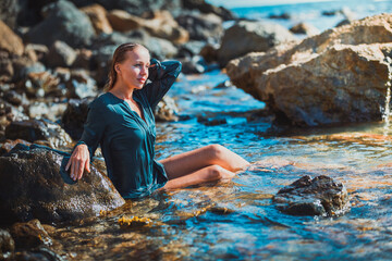 Summer time and relaxation concept. Woman in blue wet dress sitting in crystal sea water. Meditation and time for relax