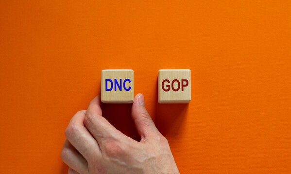 Symbol for the election in the United States. Hand picks a cube with the acronym DNC. Beautiful orange background, copy space. Political concept.