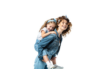side view of laughing mother piggybacking daughter in denim outfit isolated on white