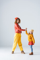 mother and daughter in colorful red and yellow outfits holding hands on grey background