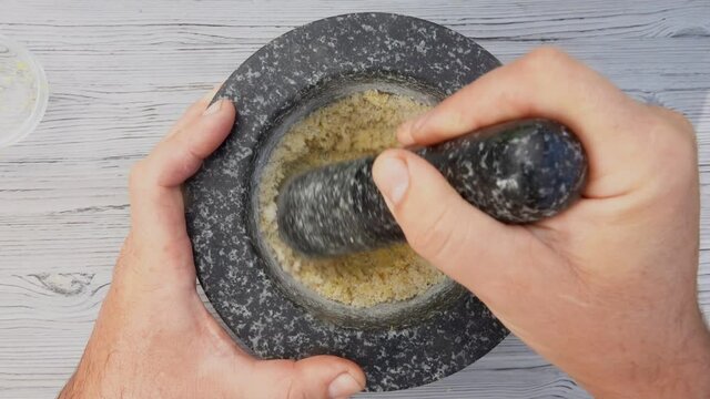 Male hand is grinding sea salt, lemon and brown sugar in the mortar with a pestle