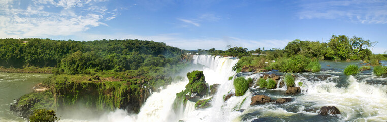 Fototapeta na wymiar Large nature panorama of Iguacu (Iguazu) waterfall cascade on border of Brazil and Argentina. Amazing view of falls Cataratas in bright Sunny weather. Concept of travel. Copyright space for site