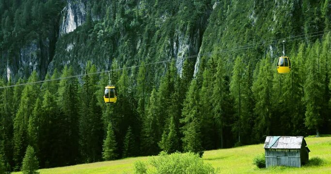 Cable car going up in summer. It is surrounded by green pine tree forest and mountains under the sunlight - aerial view with a drone 4K