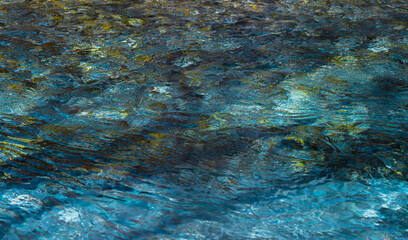 The natural background of the clear emerald green water flows in Kamikochi, Japan. The shallow level makes it possible to see the black and white rocks below. Feeling fresh, relaxed, and cool.