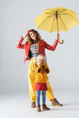 mother and daughter in colorful red and yellow outfits with umbrella and book on grey background