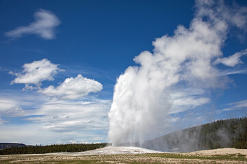 Original photograph of the Old Faithful geyser erupting in Yellowstone National Park against a beautiful blue sky.