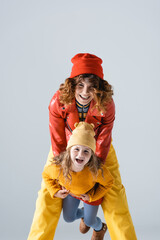 mother and daughter in colorful red and yellow outfits smiling isolated on grey