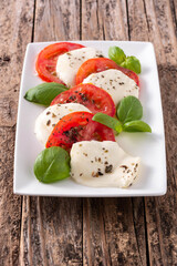 Traditional caprese salad with tomato and mozzarella cheese on rustic wooden table