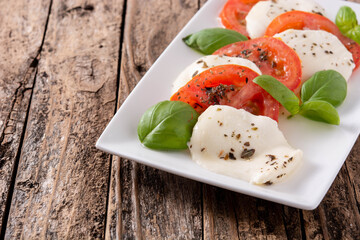 Traditional caprese salad with tomato and mozzarella cheese on rustic wooden table