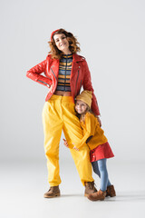 daughter in colorful red and yellow outfit hugging mother leg on grey background
