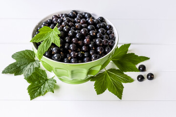 bowl with black currant on a white background. background with black currant and green leaves. black currant close-up.