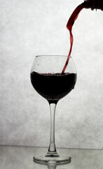 In a wine glass, standing on a white background, wine is poured from above