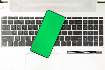 Green screen smartphone on the laptop keyboard top view